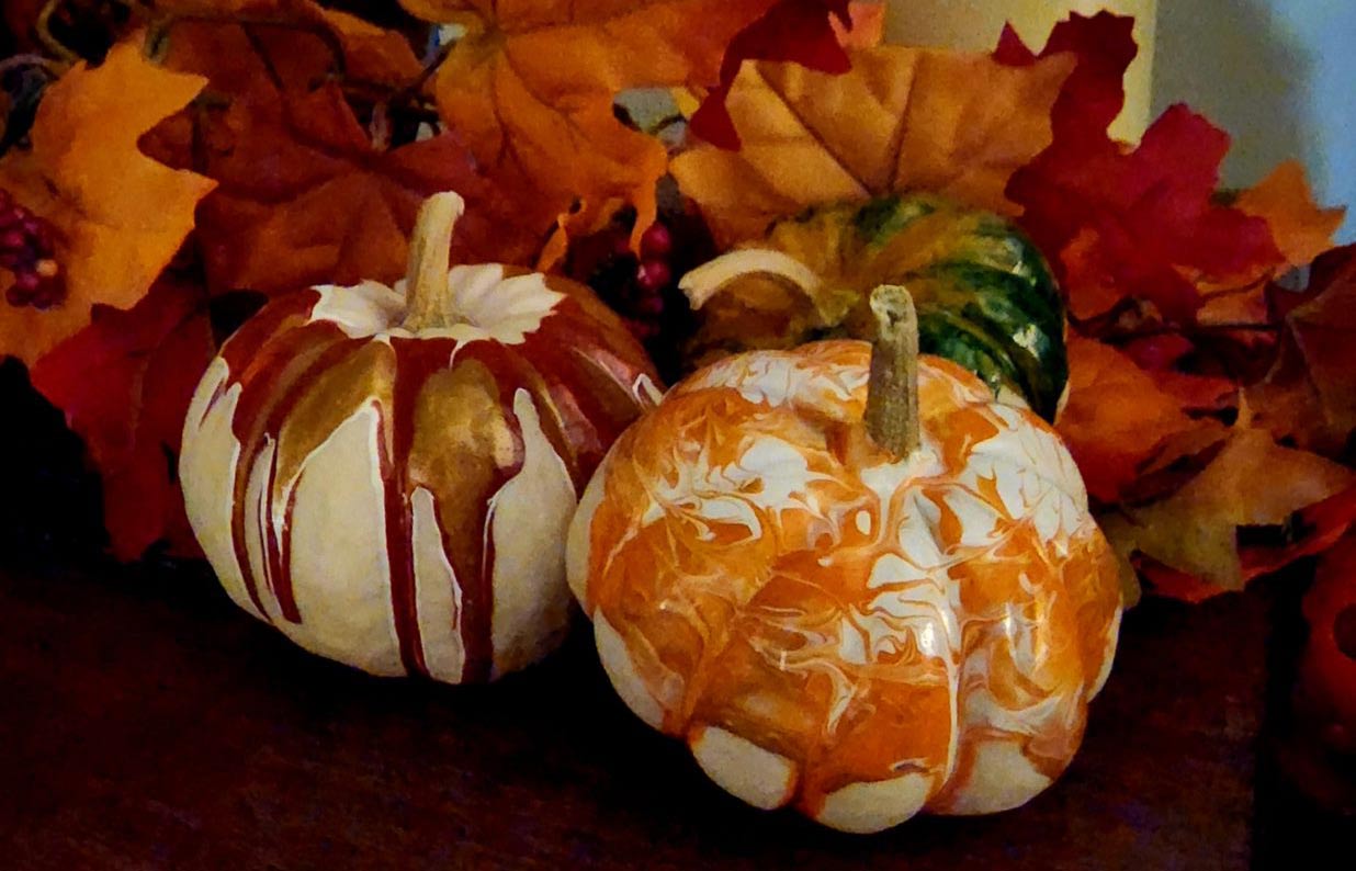 small painted pumpkins on a table with fall leaves in the background.