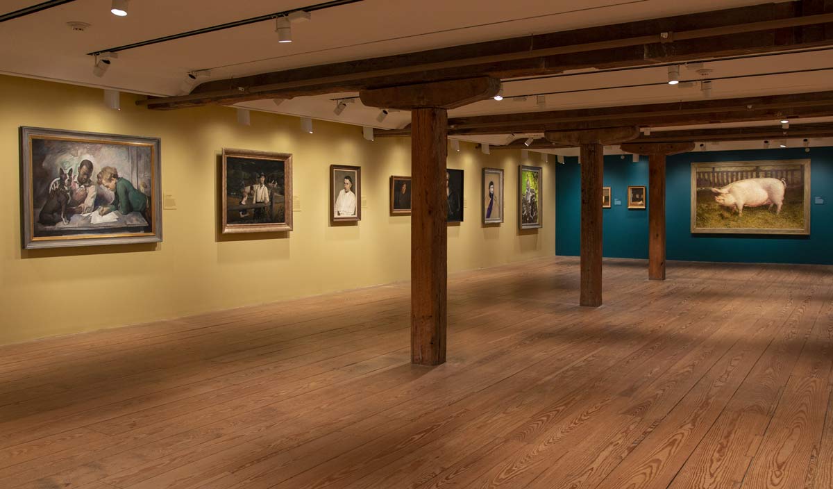 View of an art gallery with paintings on yellow and green walls.