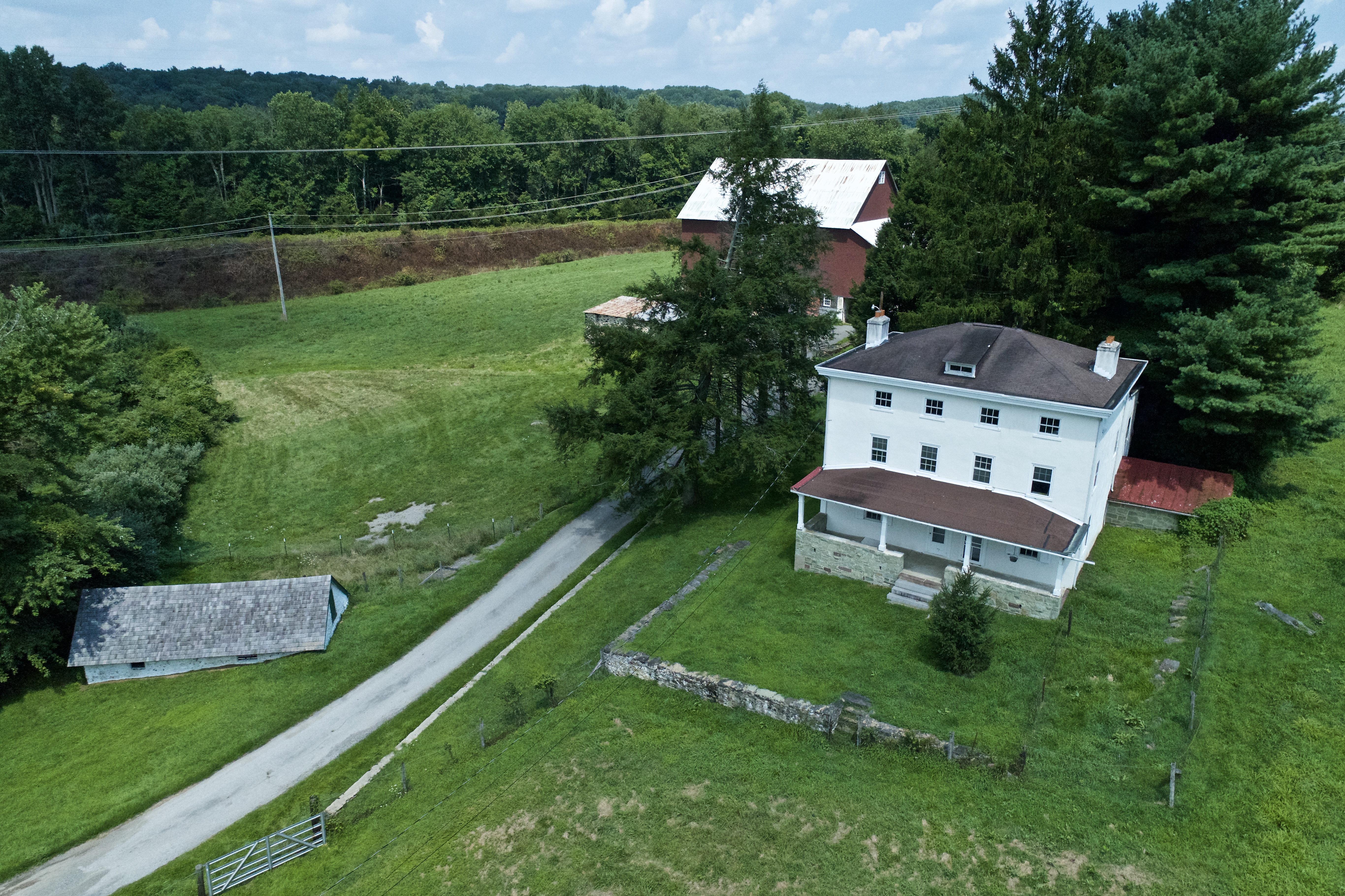 An aerial shot of a white house and red barn isolated in a field in the summer.