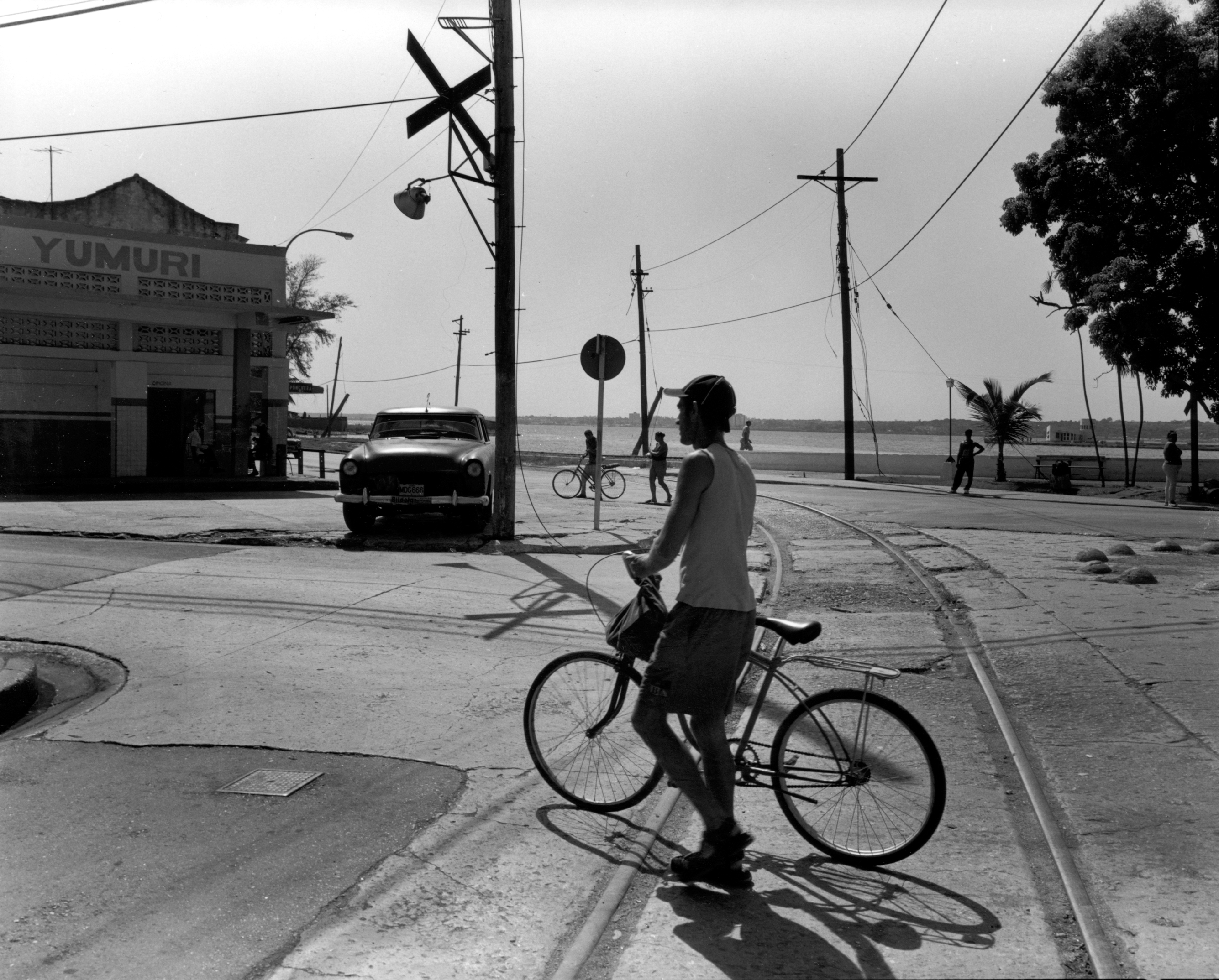 Black-and-white photograph of a boy standing next to a bike on an empty road