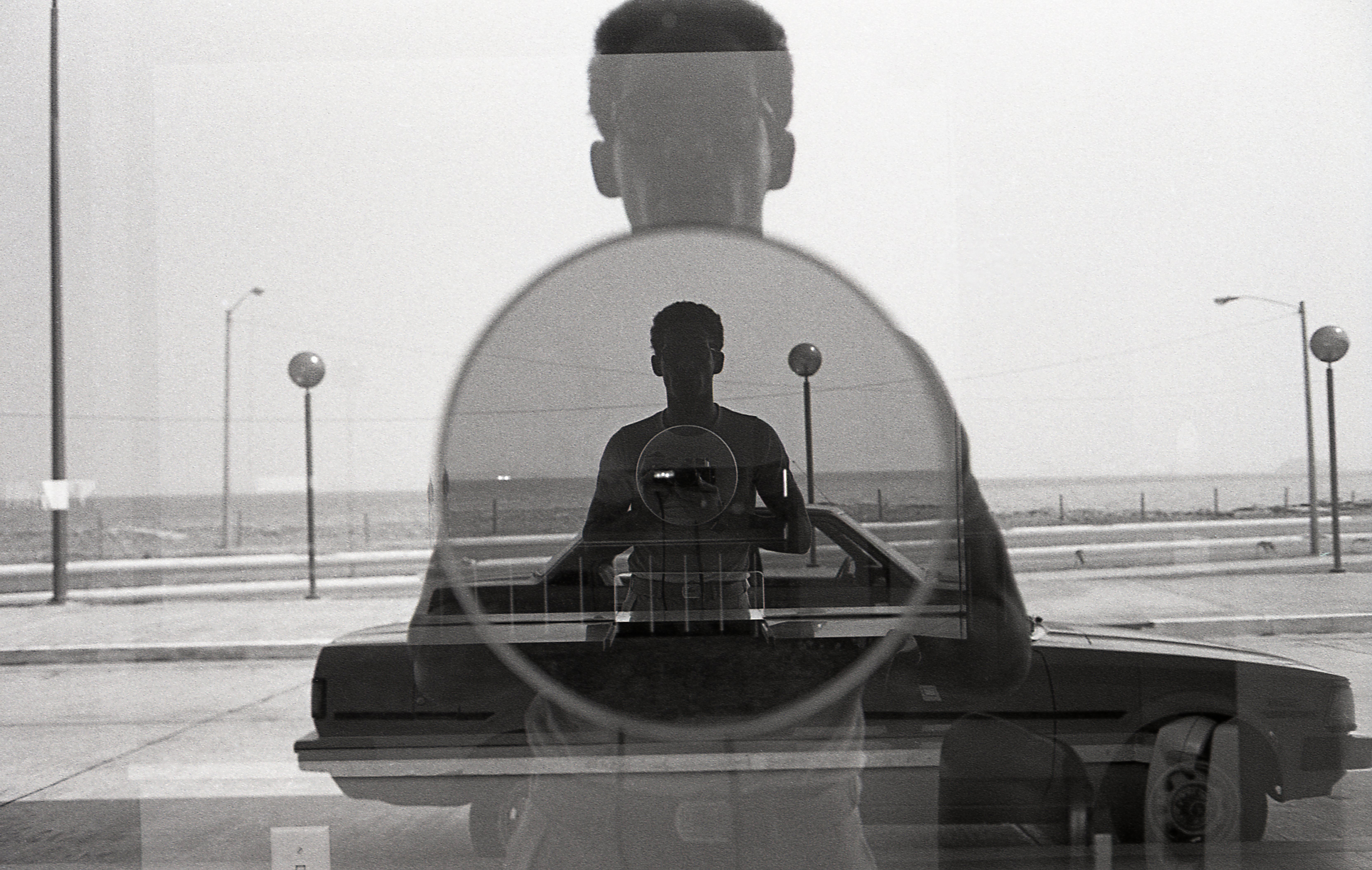 Black-and-white self-portrait photograph of a man and his reflection through a window