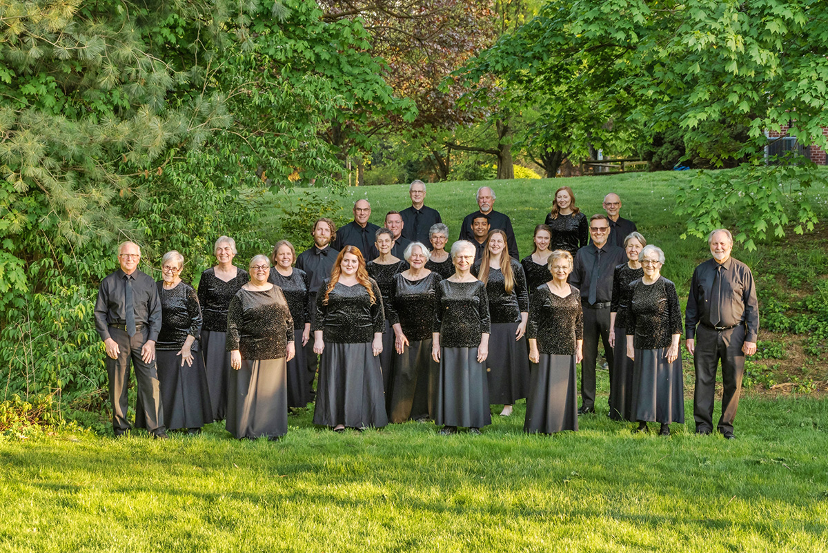 a horizontal photo of a group of people all dressed in black standing outside in a green field