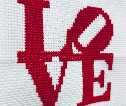 A cross-stitch pattern featuring the word "Love" in red thread on a white background