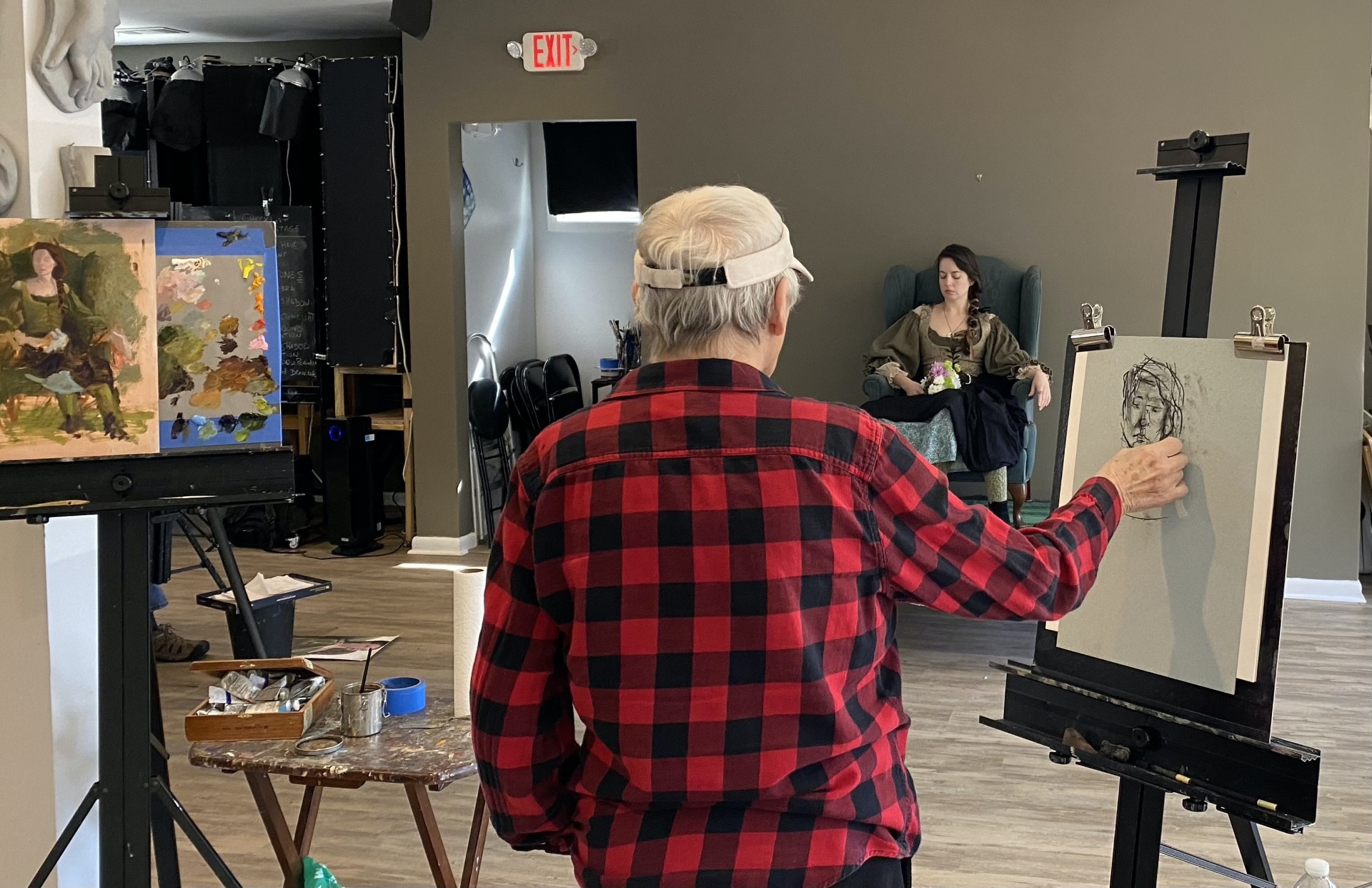 Person sitting in an art studio, sketching and looking at a subject