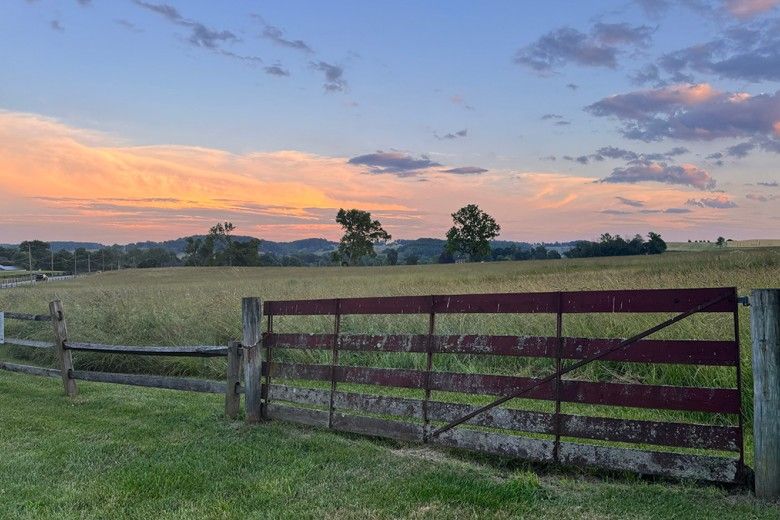 landscape photo of the sun setting on open land with a wooden fence in the foreground