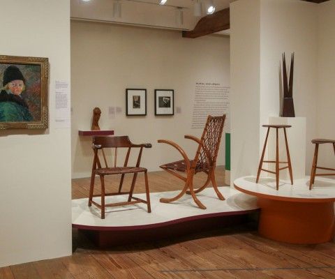 Installation view of exhibition with furniture, paintings, and prints.