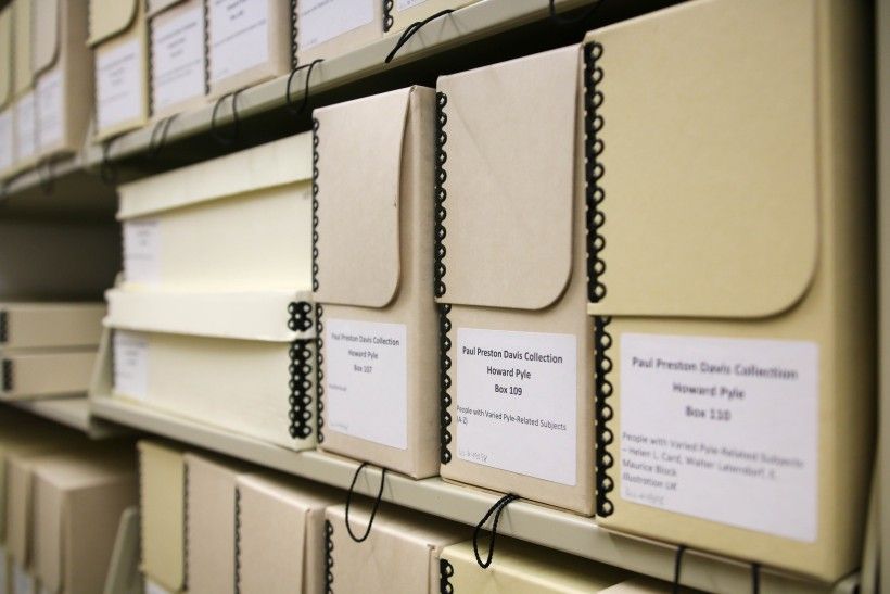 A book case filled with cardboard boxes, papers and research books.