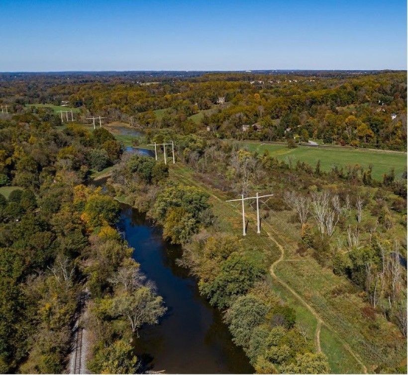 Arial view of a creek stretching through land covered in green foliage and trees