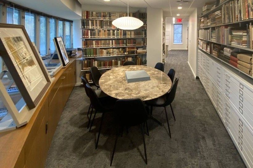 Workspace with a table and chairs in the middle, surrounded by books and prints.