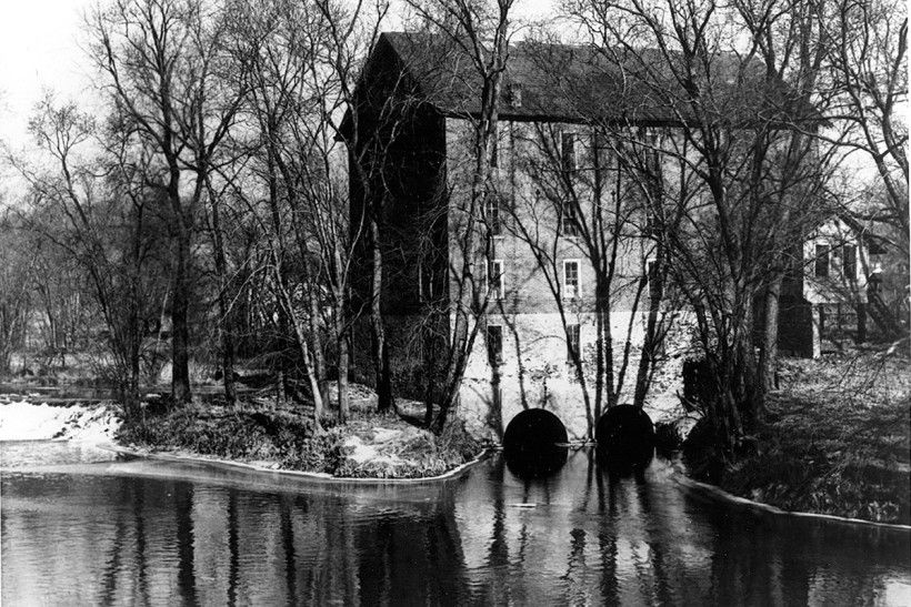 black and white historic photo of a dam creating a mill race towards a mill