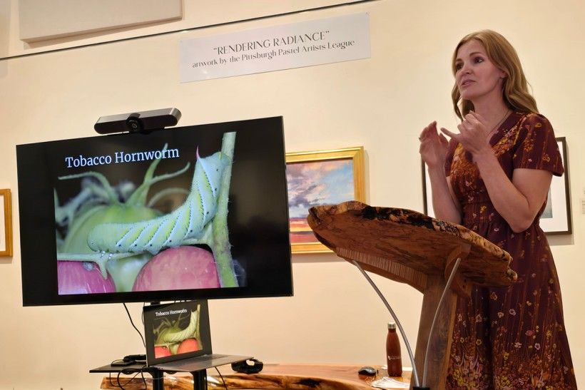 a woman stands next to a screen, giving a presentation about moths