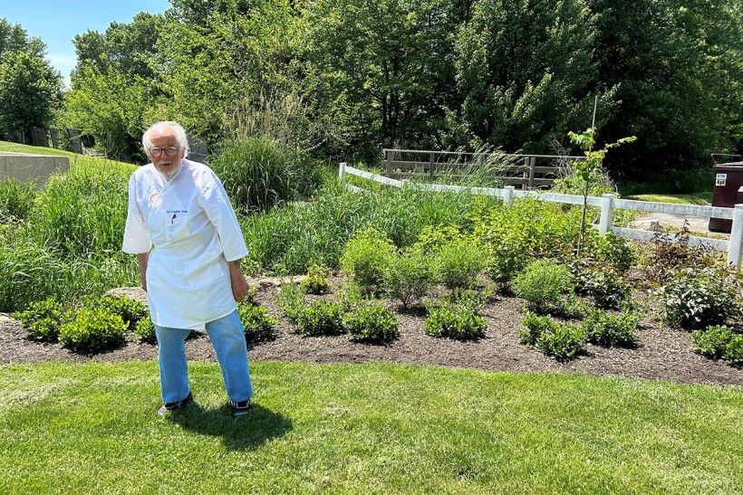 photo of a man standing outside on green grass in front of new garden plantings