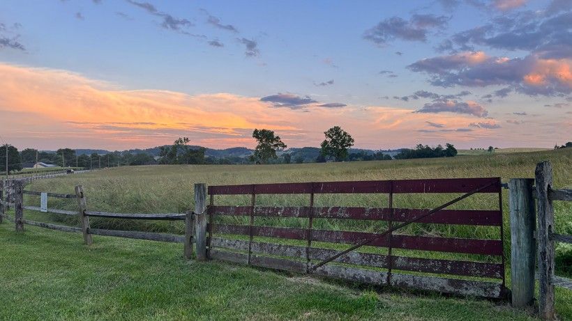 landscape photo of the sun setting on open land with a wooden fence in the foreground