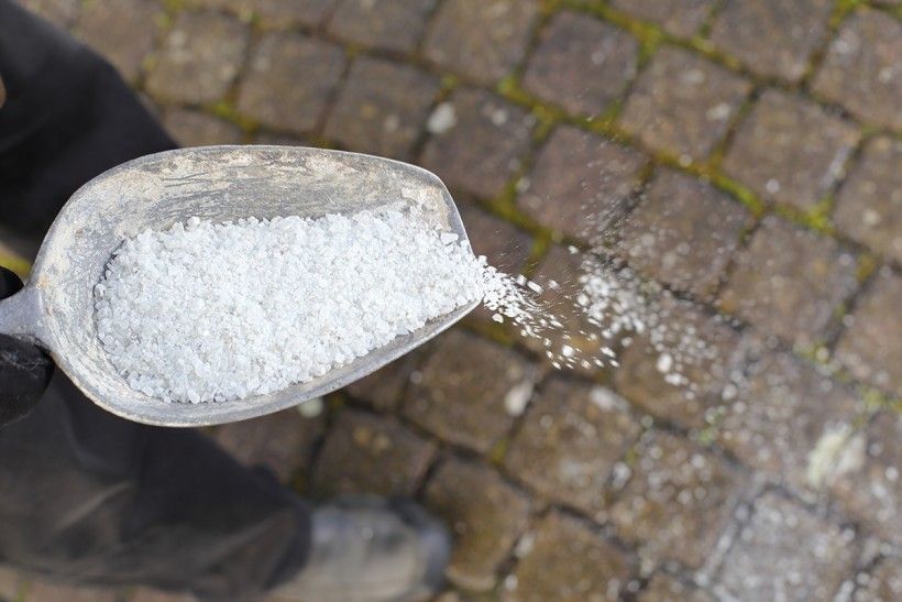 photo looking down at a large scoop filled with salt as it's getting ready to be spread on a sidewalk