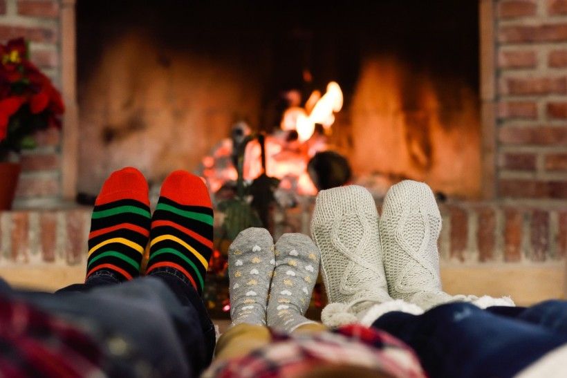 Cozy POV photo showing three pairs of feet, cozy in socks, being warmed by a fireplace.