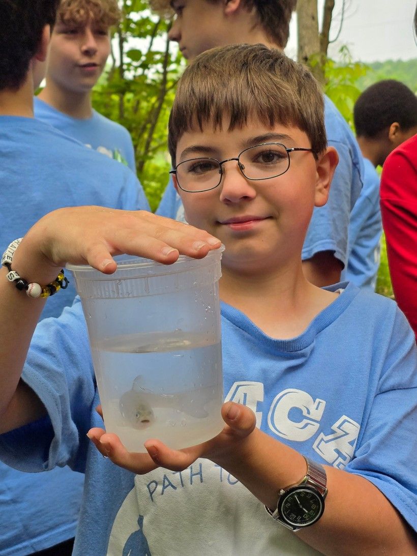 a young boy holds up a tall clear container holding a fish in water ready to be released