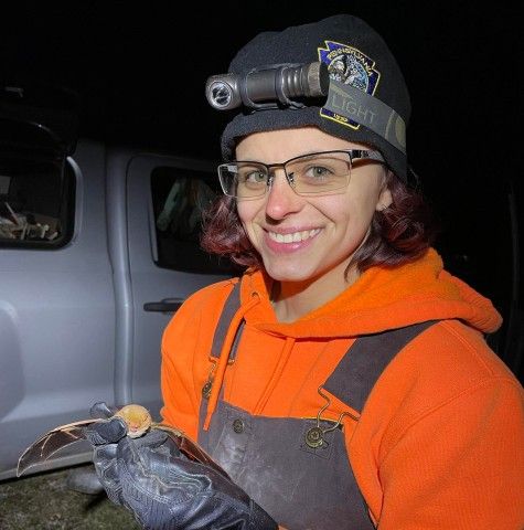 square image taken at night of a woman holding a bat in a gloved hand and smiling