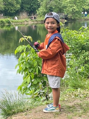 photo of a young smiling boy standing on the banks of a creek while holding a fishing pole