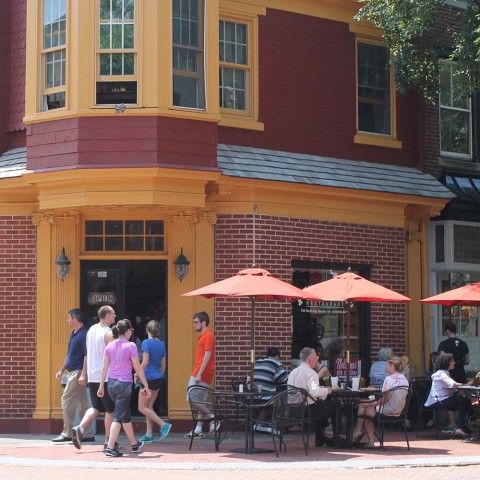 Streetscene with a couple walking in the foreground and groups dining outside a restaurant.