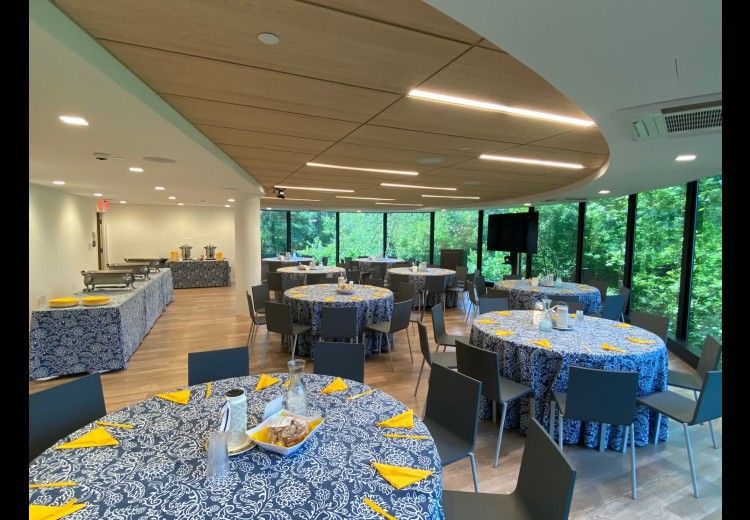 horizontal photo of tables set with blue tablecloths in a room with floor-to-ceiling window views