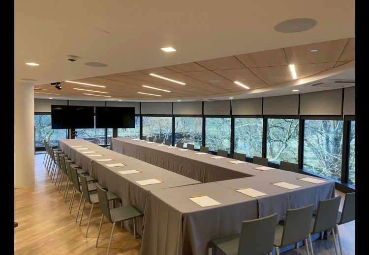 horizontal photo of long tables set up in a U-formation in a room with floor-to-ceiling window views